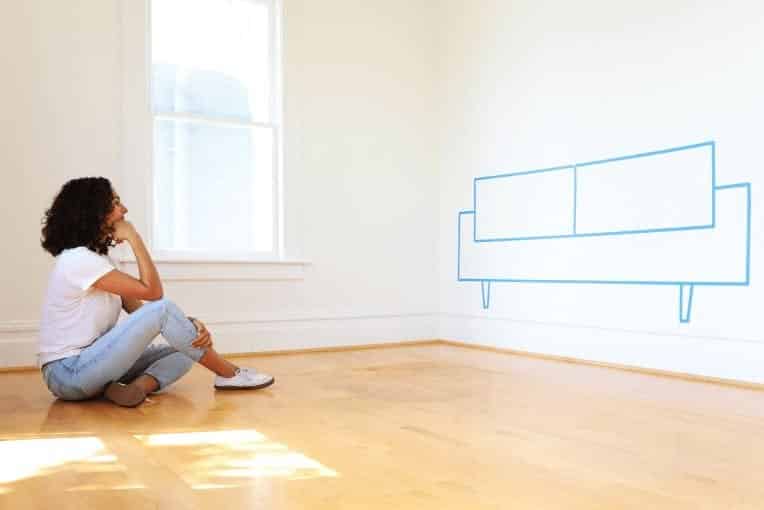 Young woman looking at a blank wall, daydreaming of a couch there